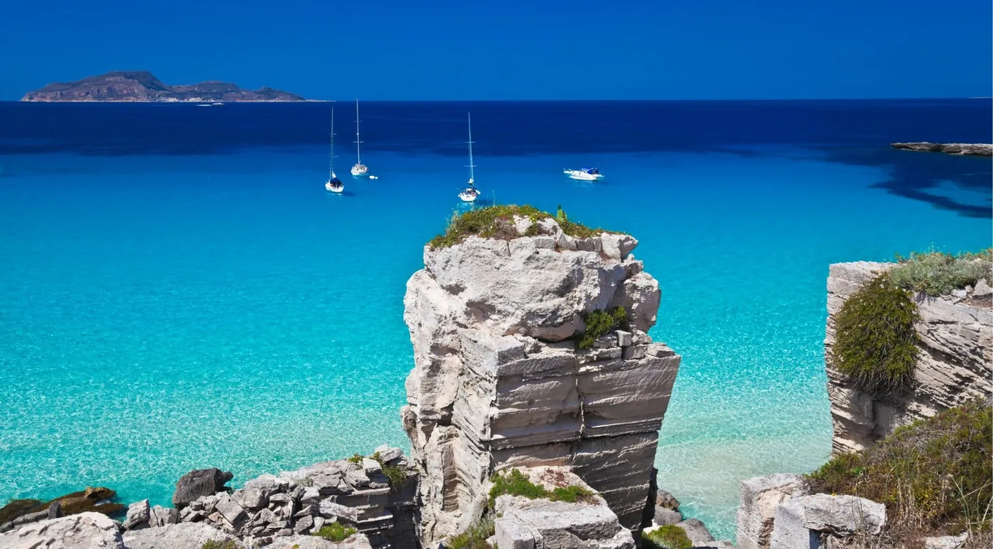 A limestone sea stack with boats anchored in deep blue water off the Egadi Islands