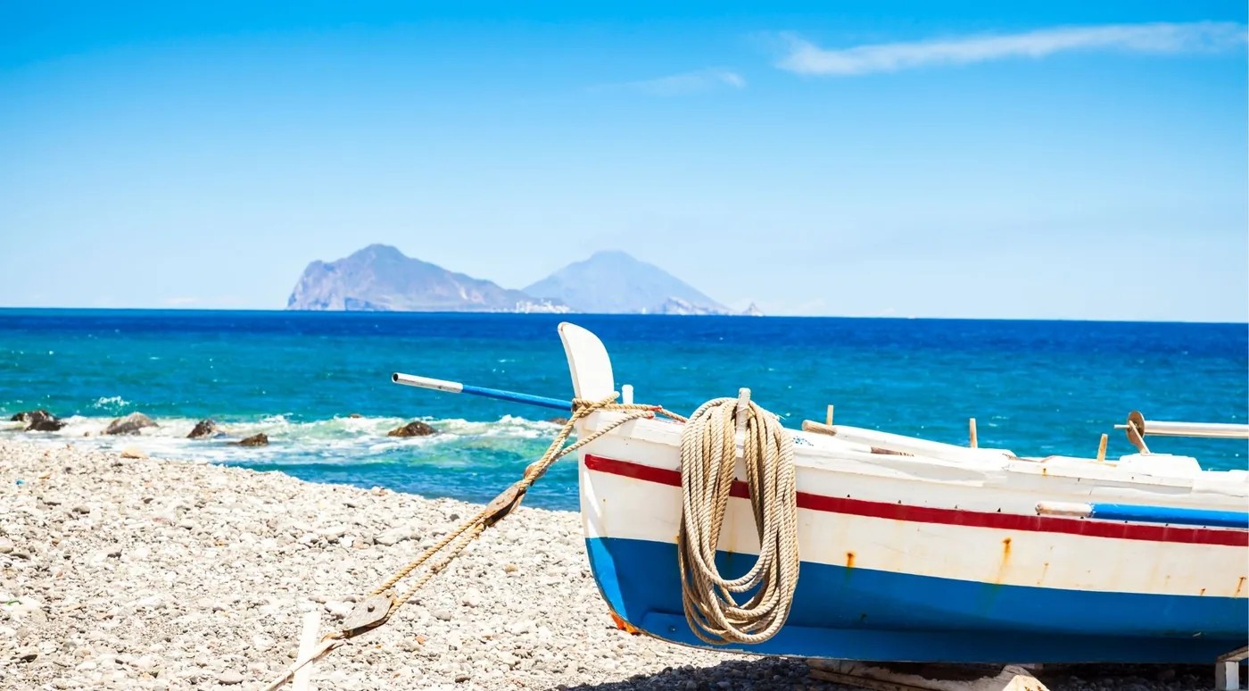 A traditional wooden fishing boat drawn up on a shingle beach with Favignana behind