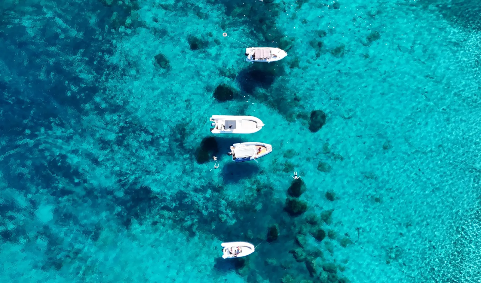 Boats anchored over bright turquoise shallows, seen from the air