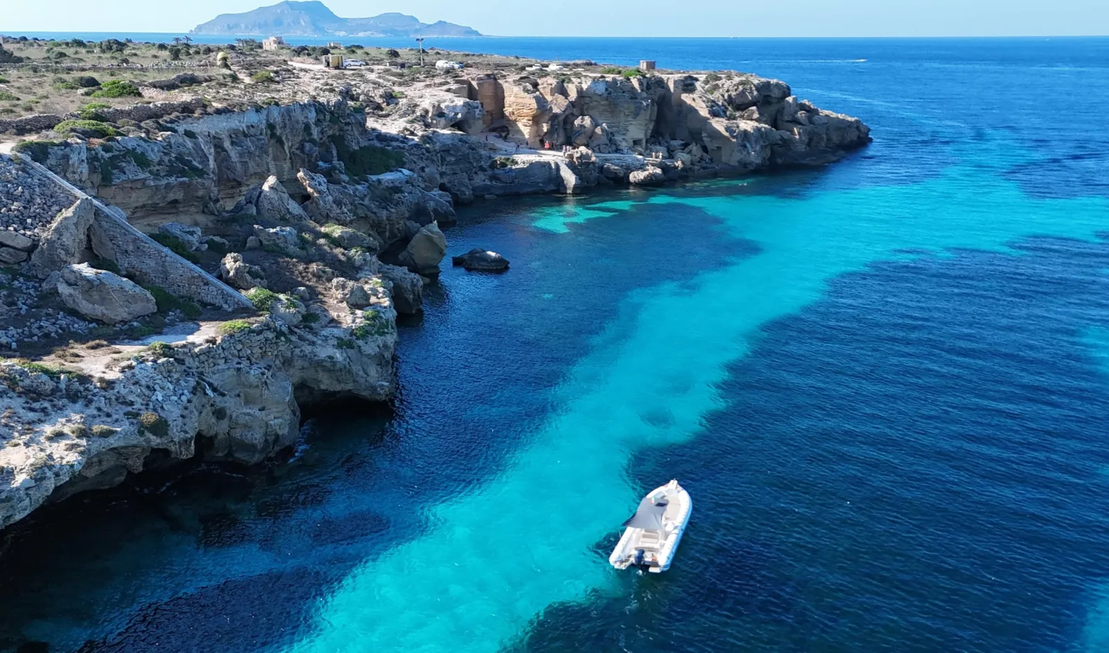 The rocky Favignana coastline with a boat anchored in the clear water below