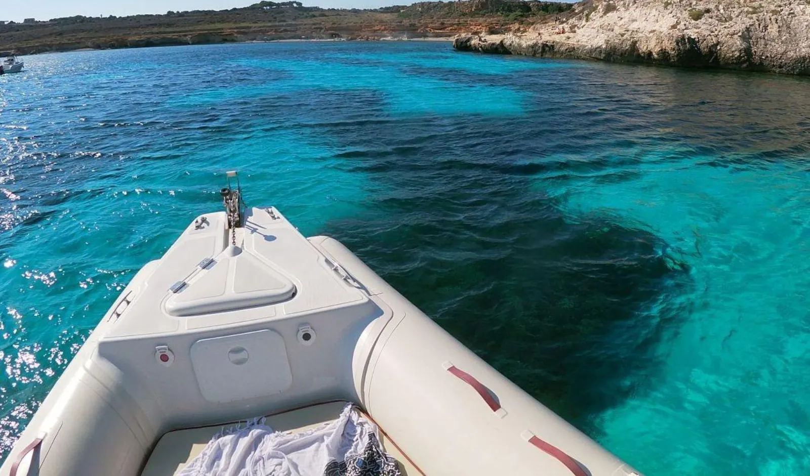 The RIB's bow at anchor above a clear turquoise seabed
