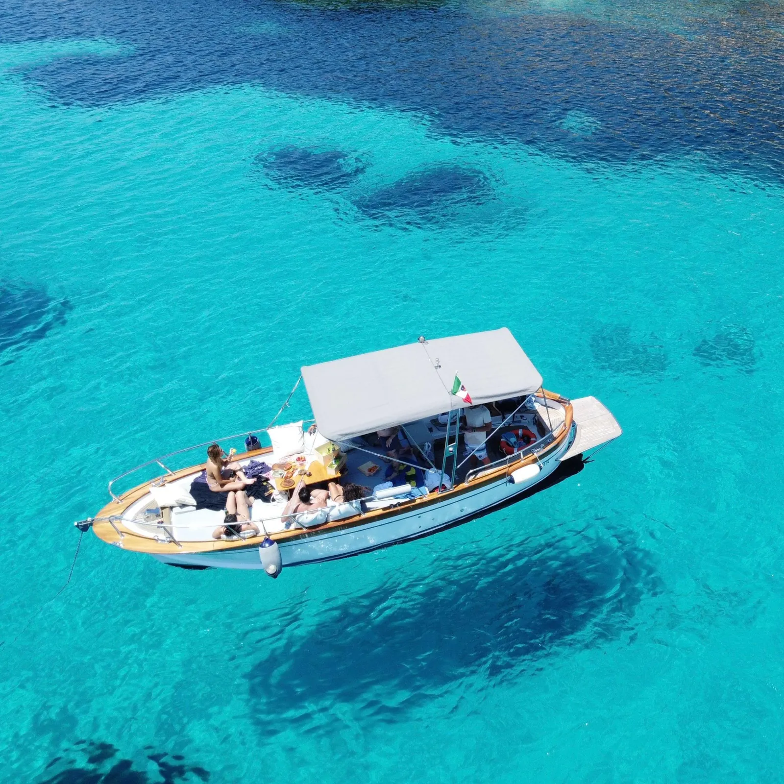 The wooden gozzo under its sun awning, at anchor in turquoise water