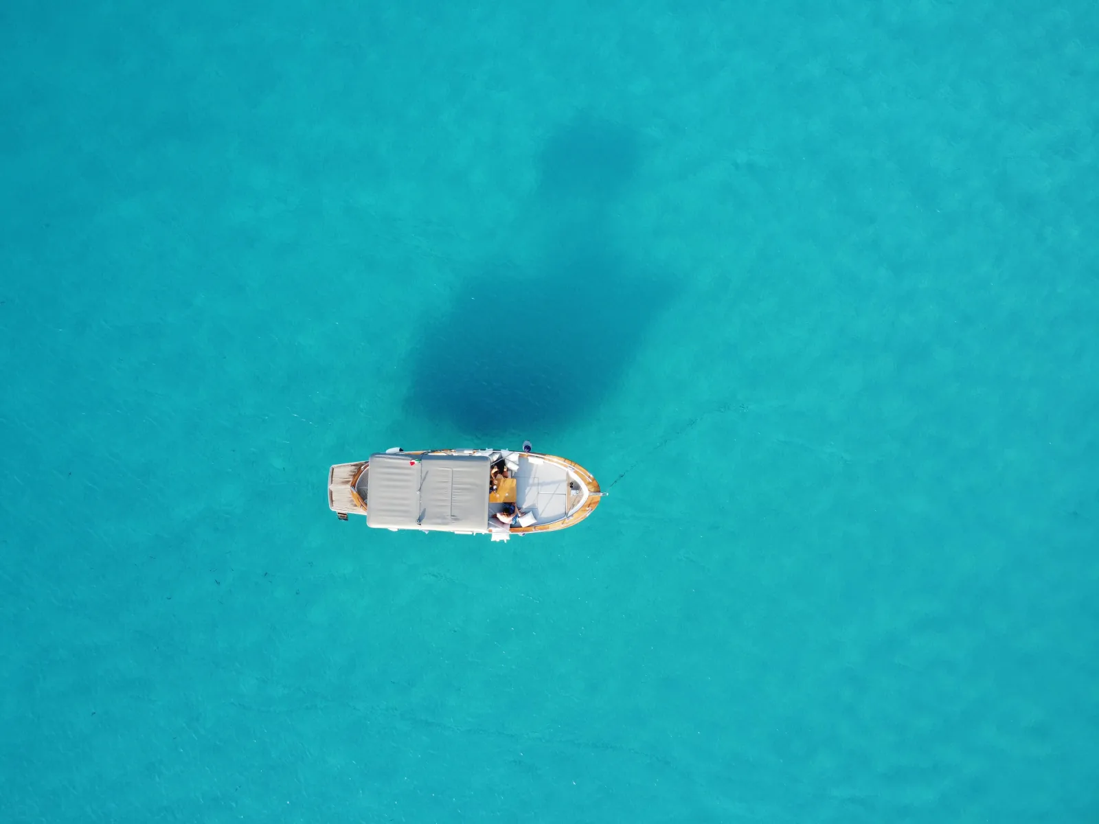 The boat on flat pale-turquoise water seen from the air