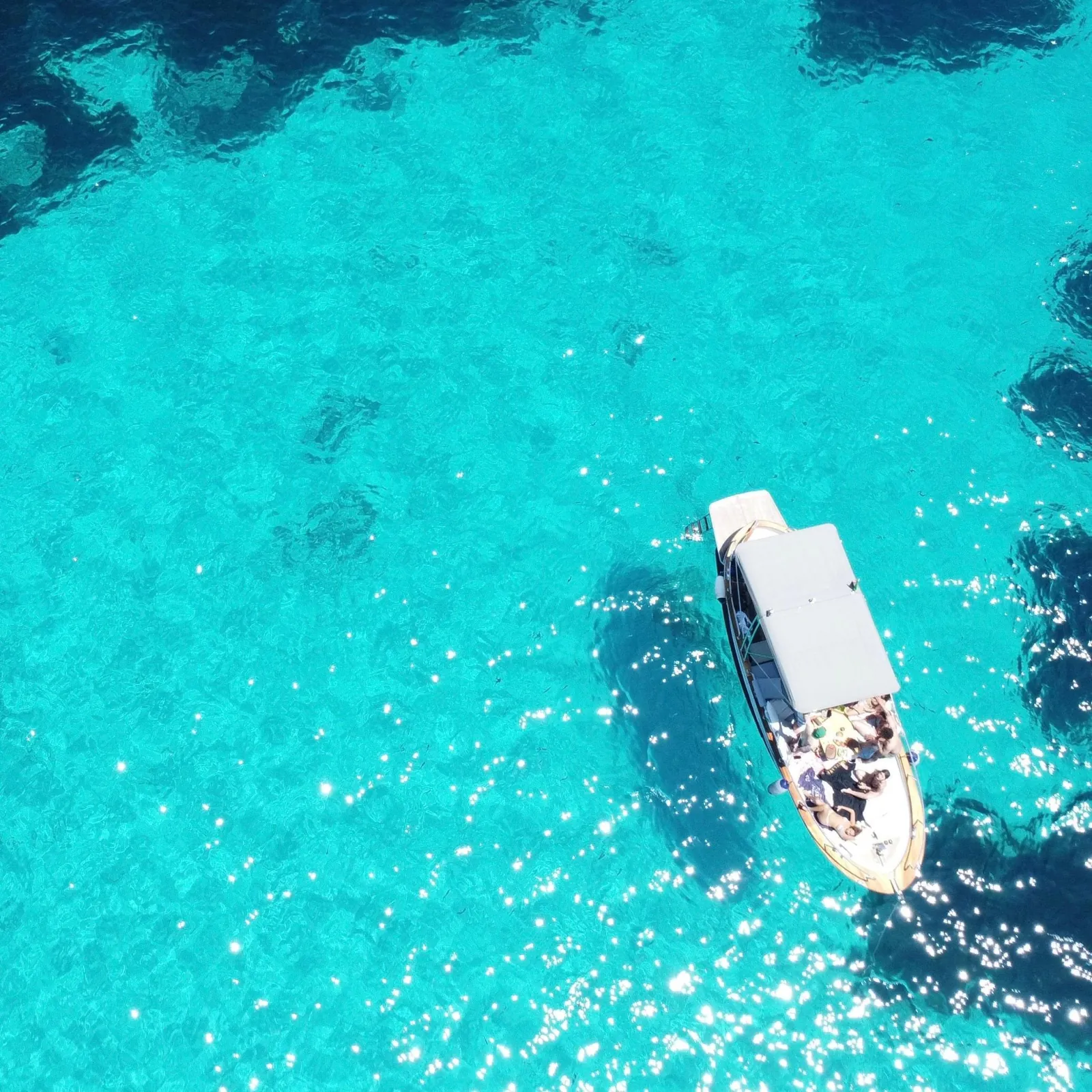 The wooden boat on sunlit turquoise water, seen from overhead