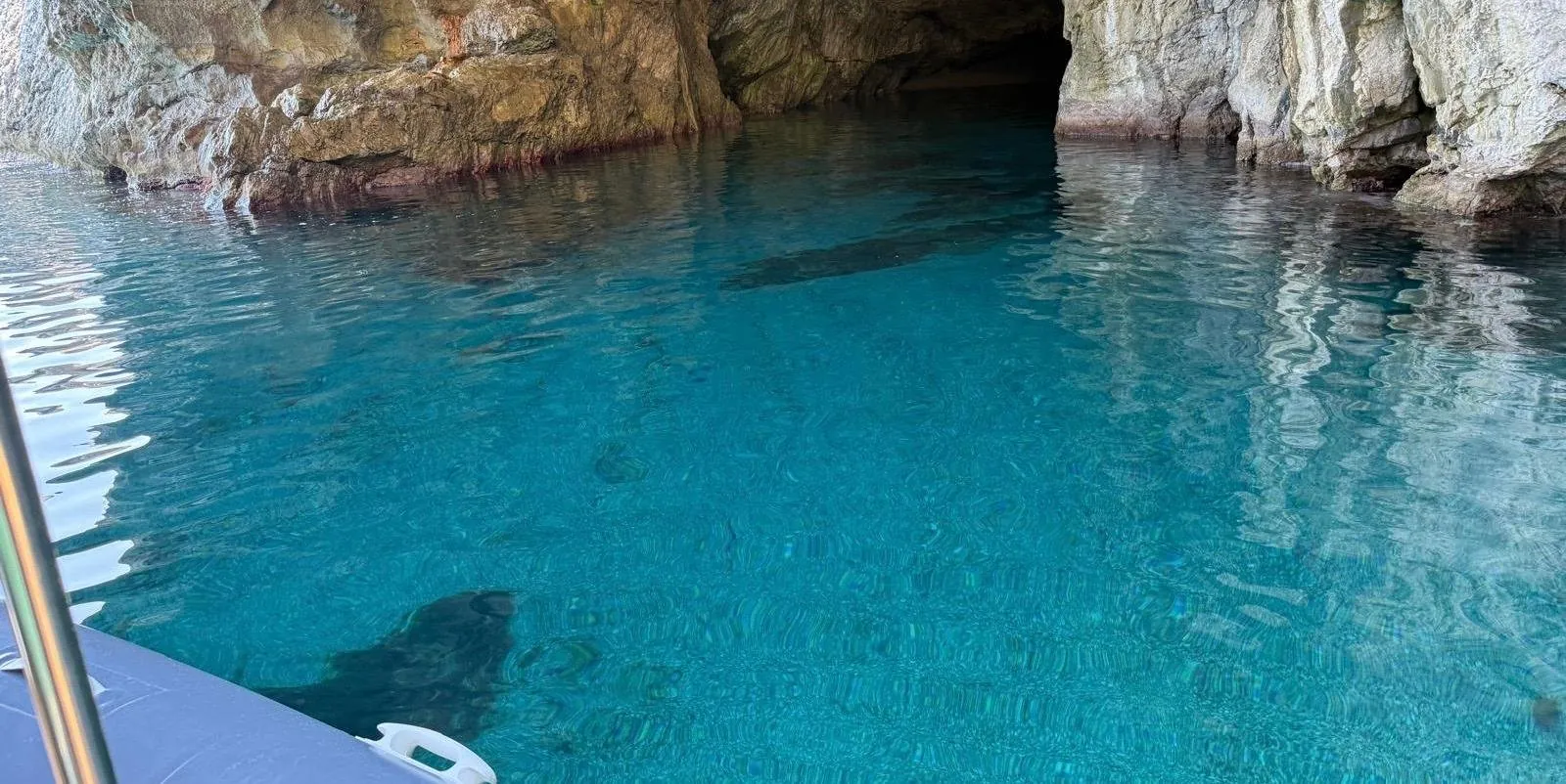 The boat's bow inside a sea cave, light on the turquoise water