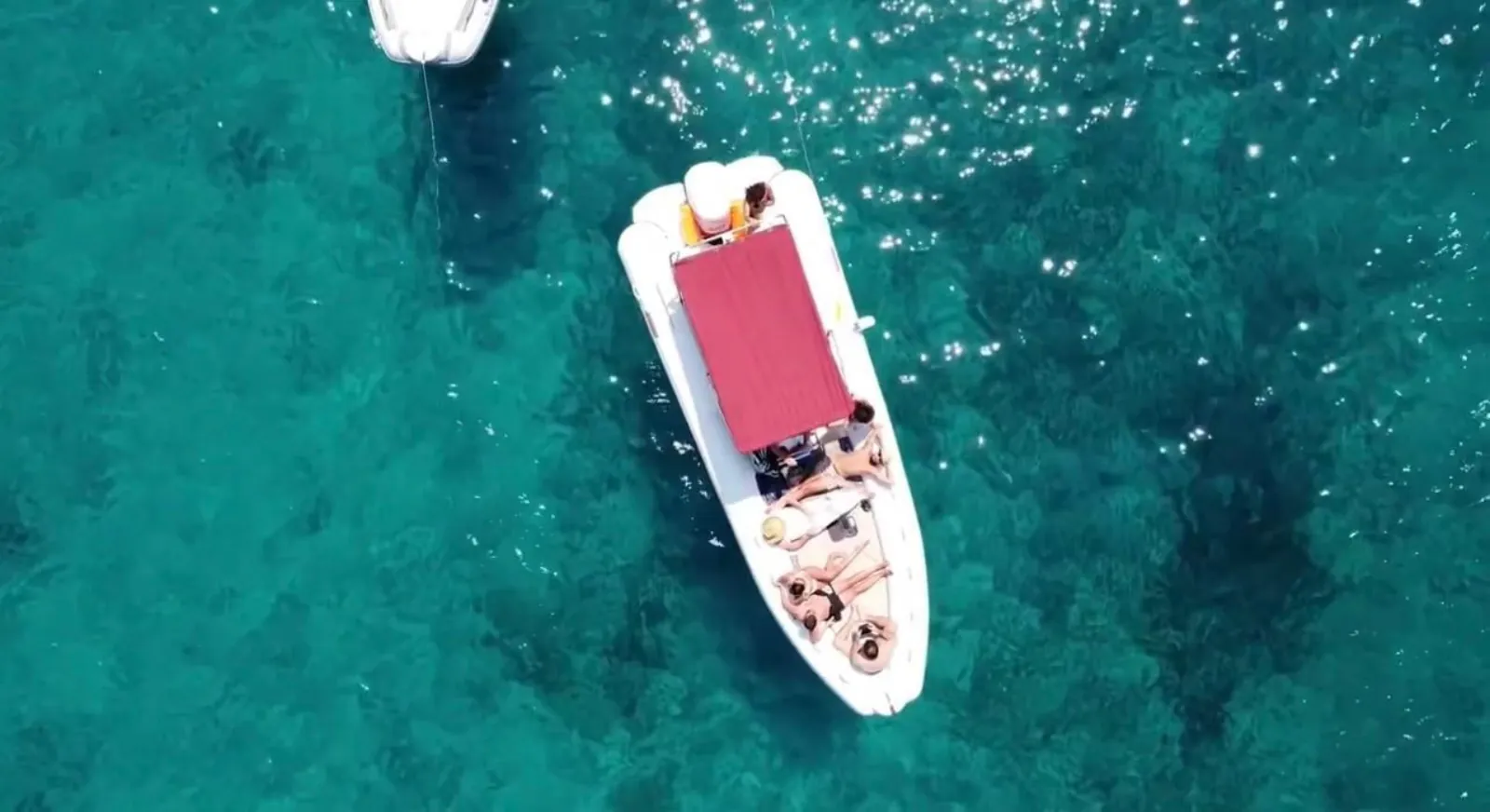 The RIB from overhead, guests sunbathing on its red foredeck cushion