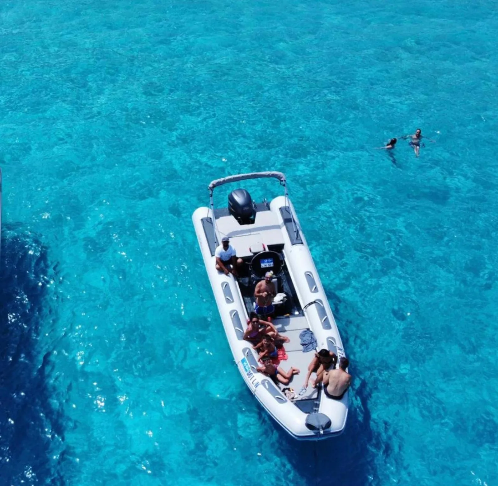 The RIB anchored over pale turquoise sand with a swimmer nearby