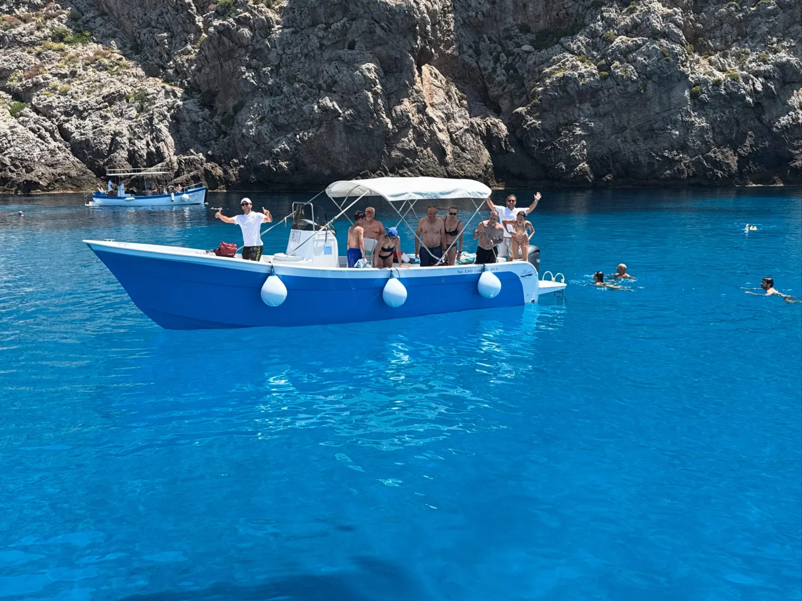 The blue wooden-hulled boat at anchor with guests swimming around it