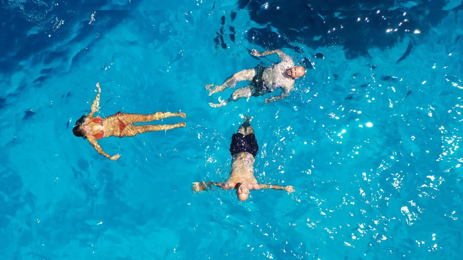 Three snorkellers floating in bright turquoise water, seen from above