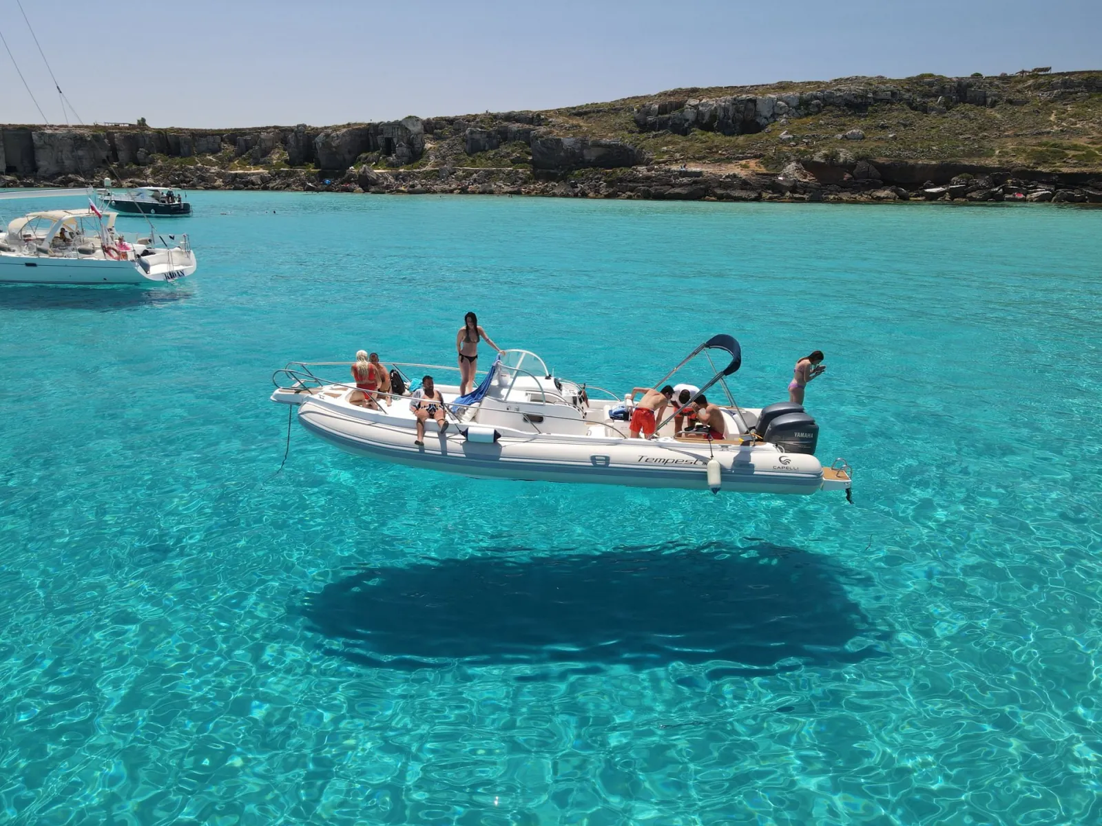 Guests aboard the boat in a shallow bay with the low Favignana coastline behind