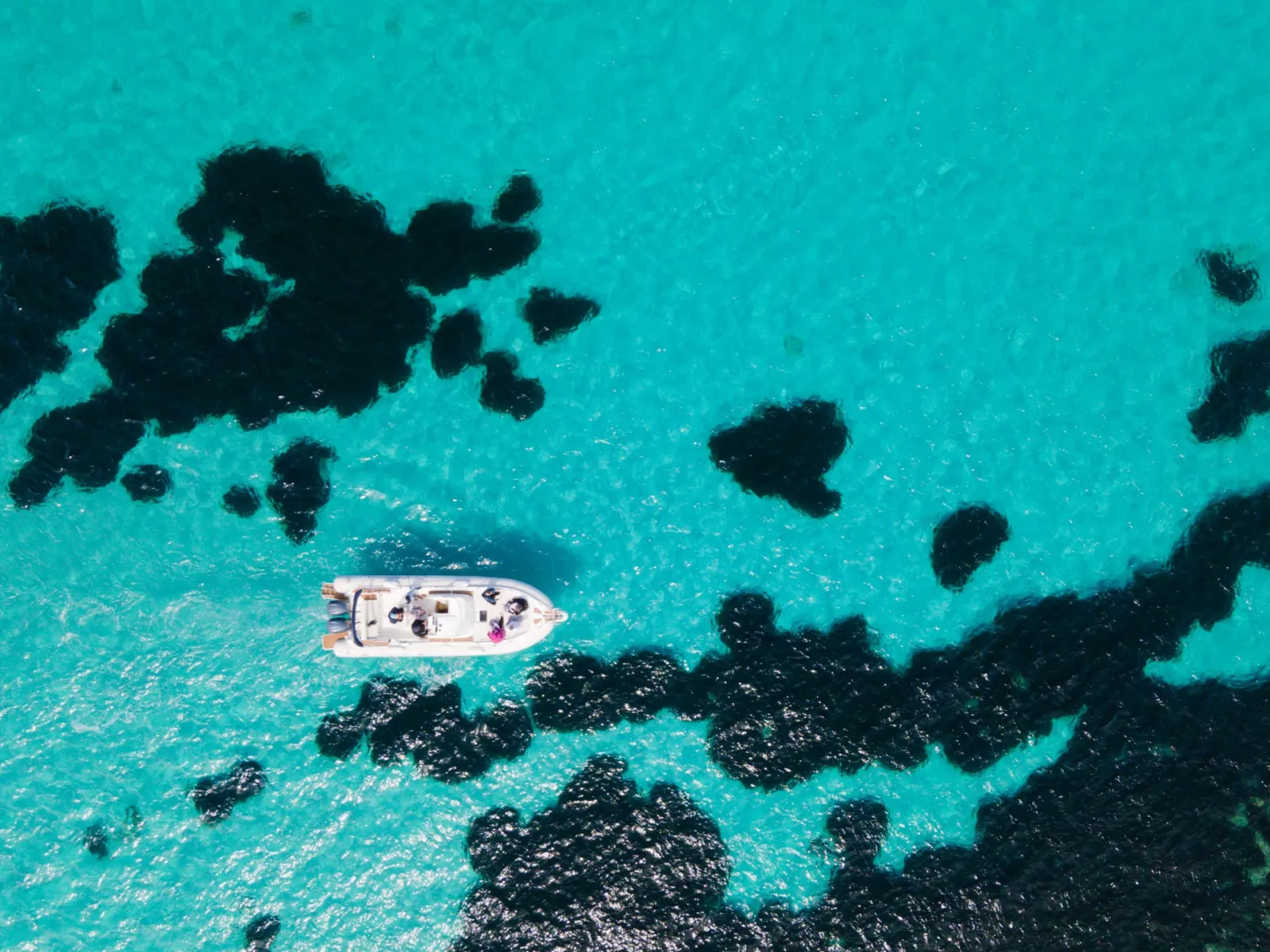 The boat anchored among dark seagrass patches in turquoise water, photographed from the air