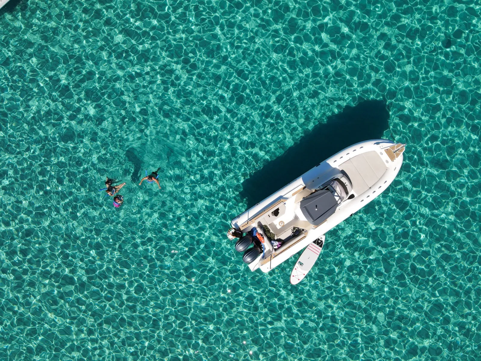 The boat at anchor from overhead with snorkellers swimming out from its stern