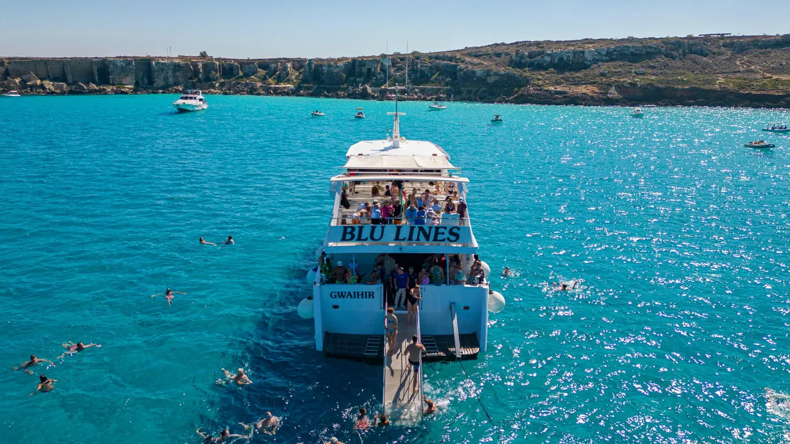 The Blu Lines excursion vessel at anchor with dozens of swimmers in the water around it
