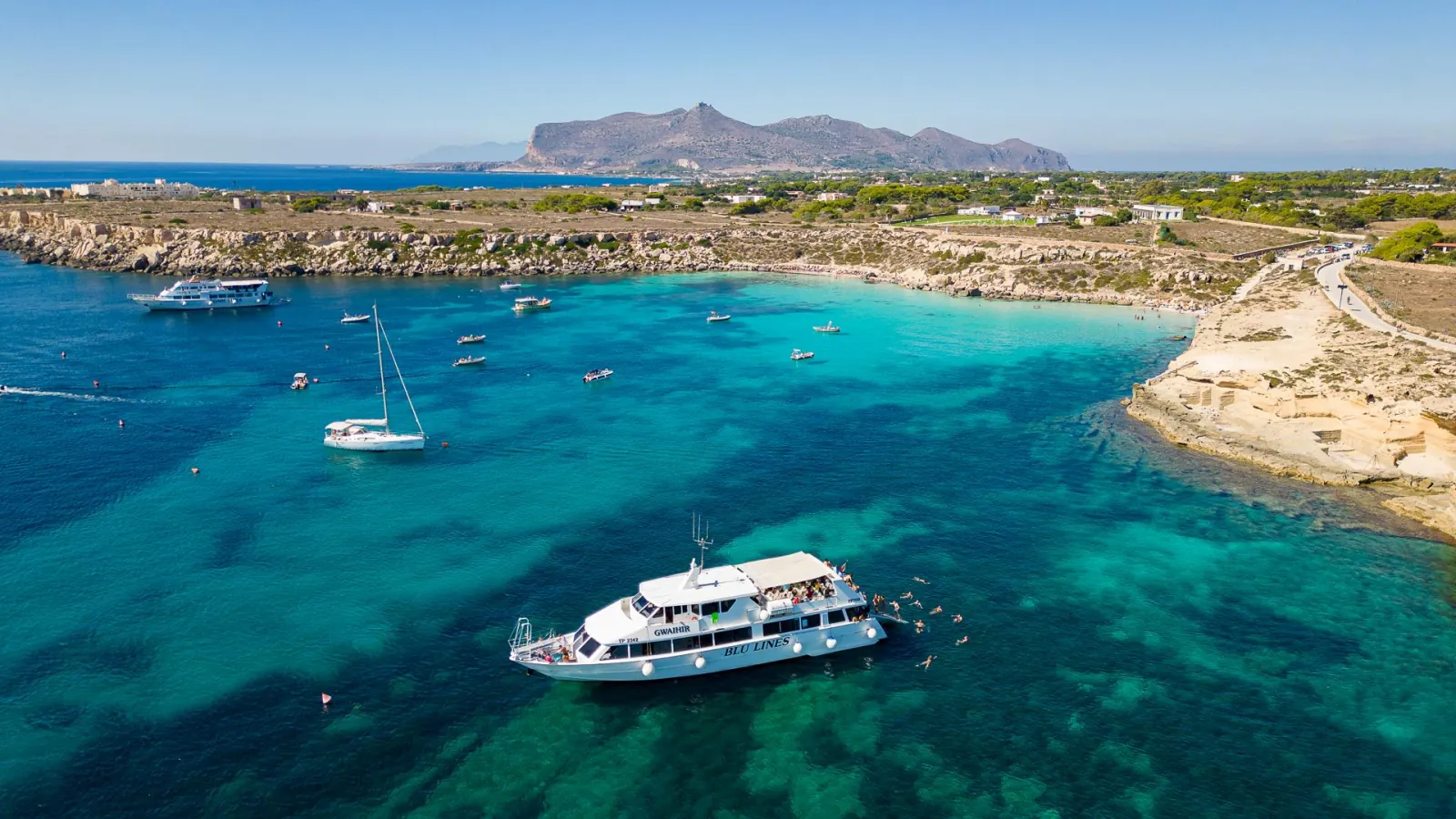 A wide Favignana bay with the excursion boat anchored and the island's mountain ridge behind