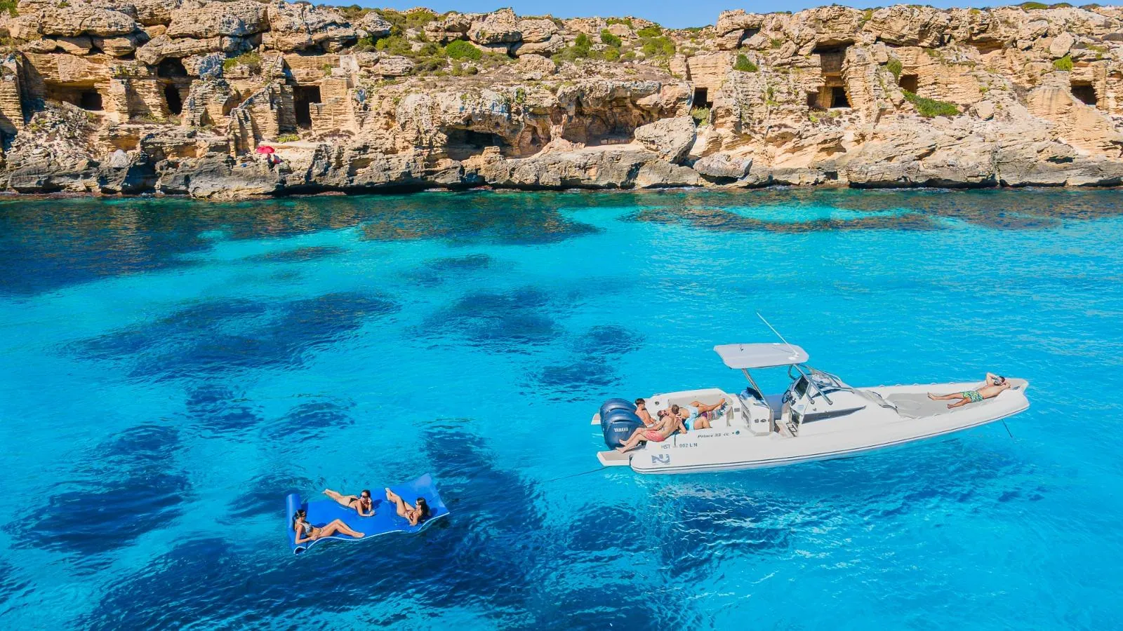 The boat anchored beneath Favignana's cut tuff cliffs, a guest resting on the floating mat