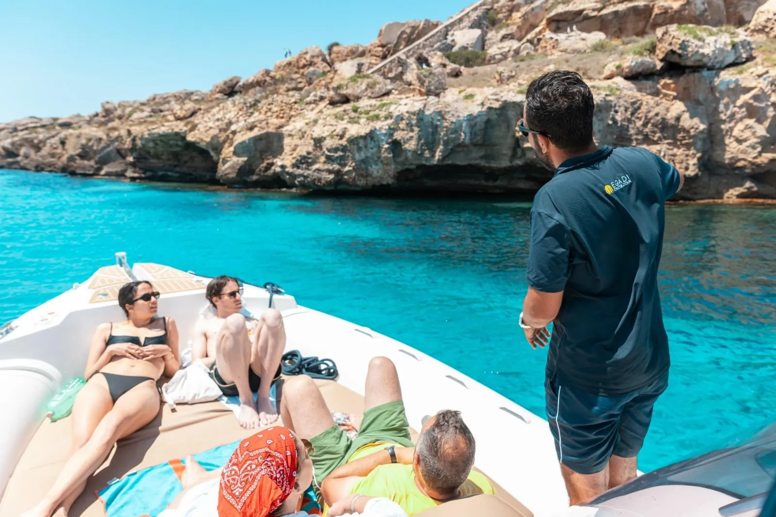 Guests relaxing on the foredeck while the skipper stands at the rail in a rocky cove