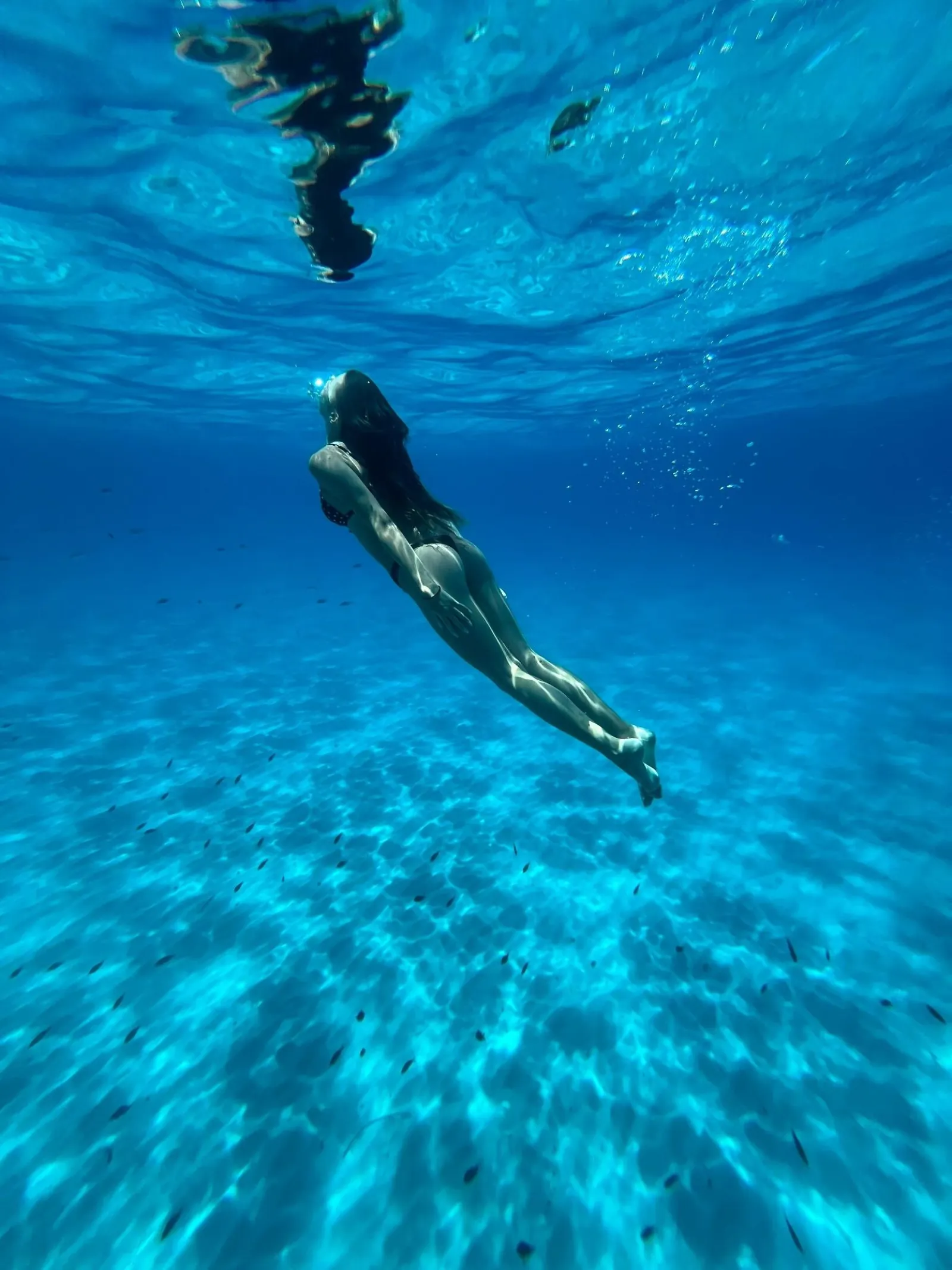 A swimmer underwater in clear blue water beneath the boat