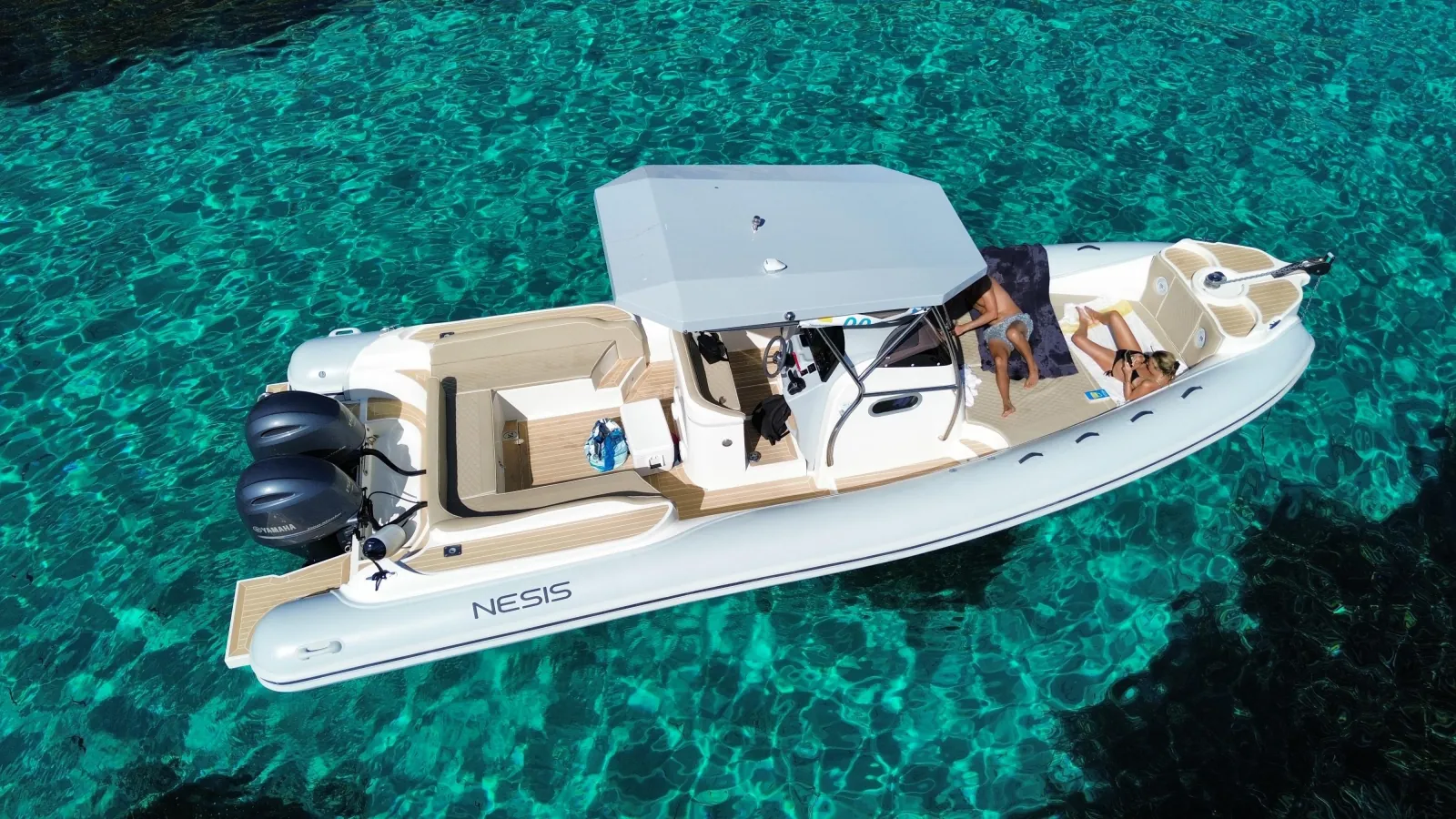 A white maxi-RIB with a sun canopy and guests aboard, anchored in clear turquoise water off Favignana