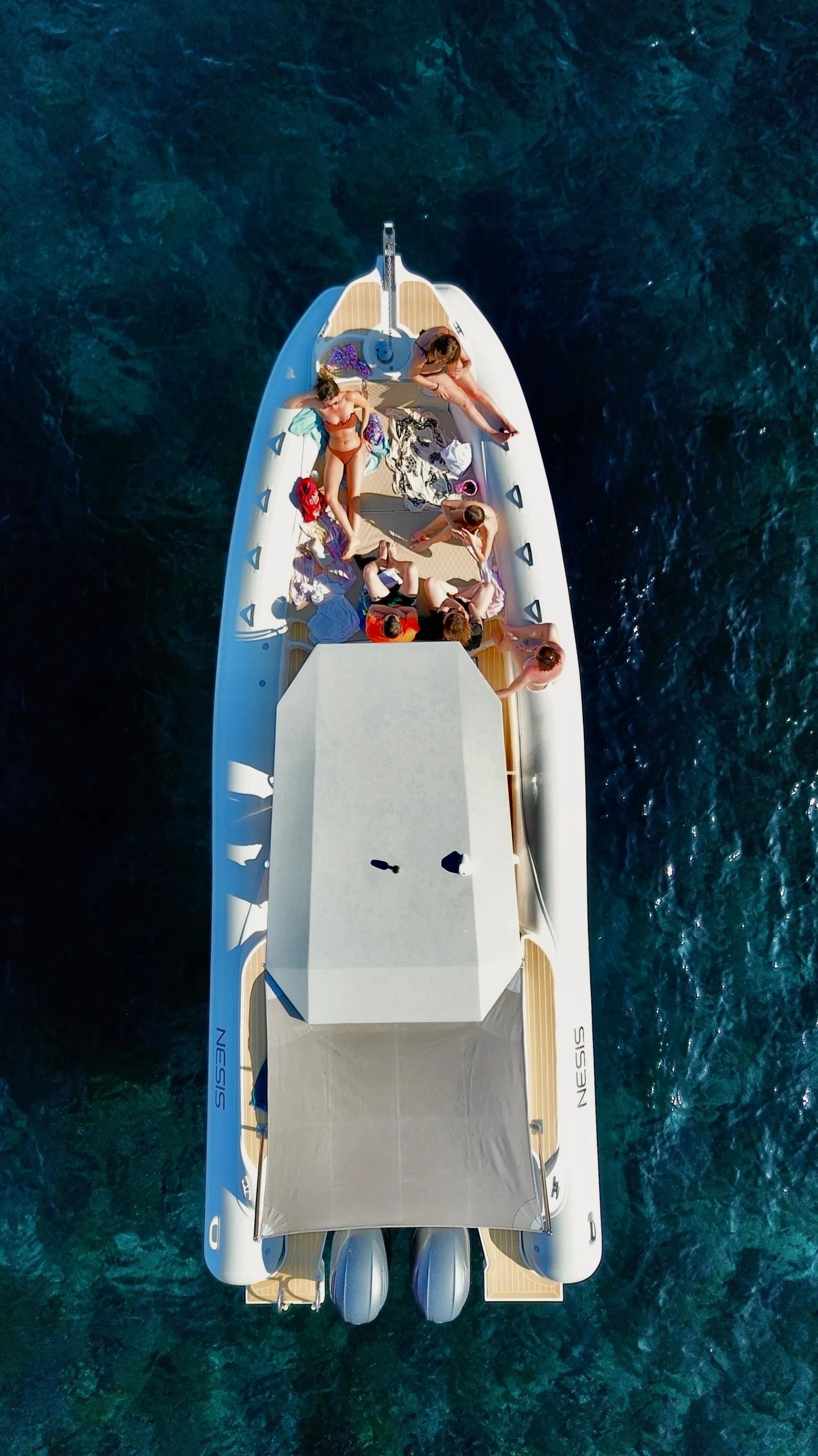 The maxi-RIB's foredeck sunbathing pad seen from above, guests lying out at a swim stop