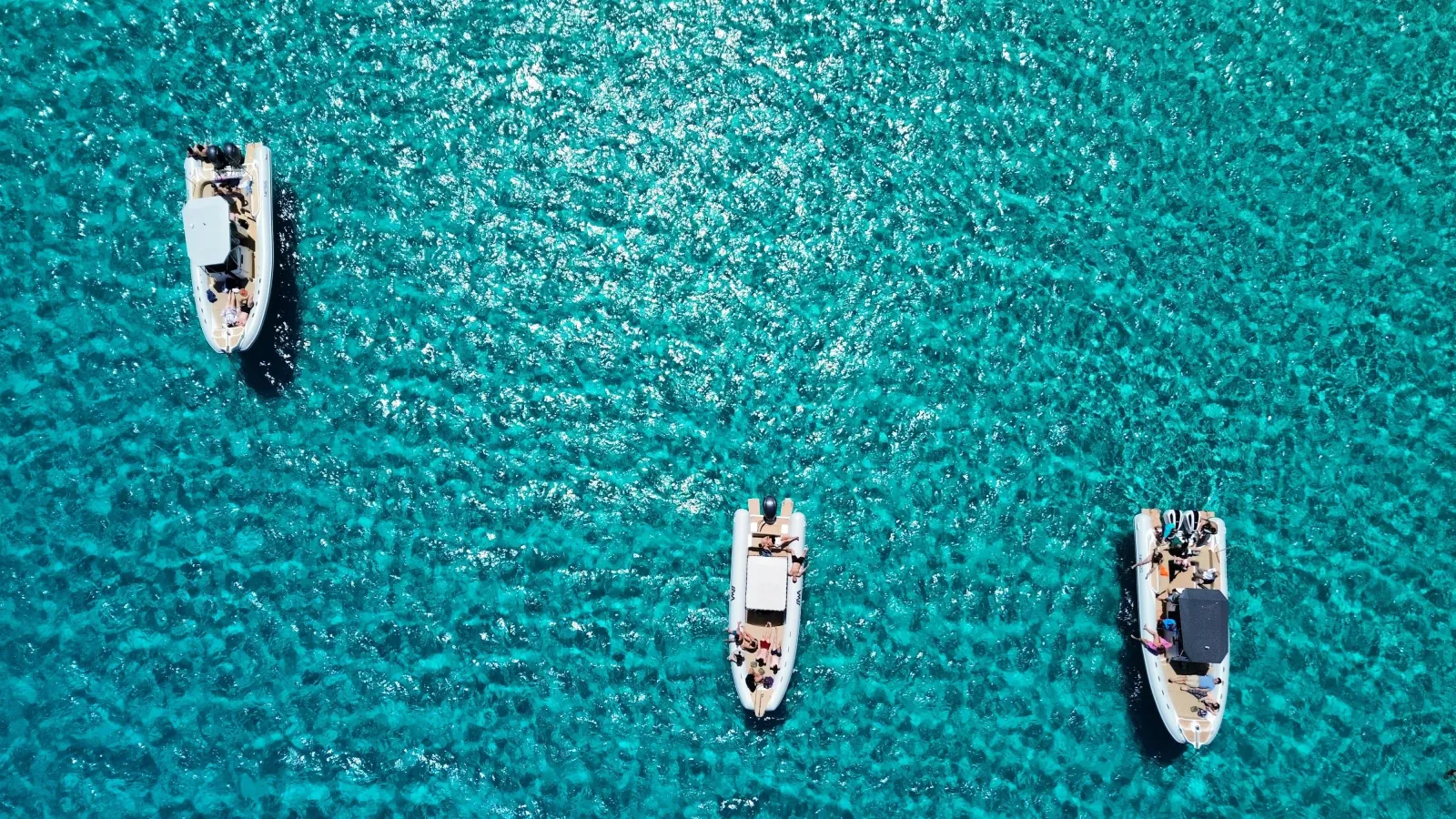 Three RIBs anchored side by side over pale sand off Favignana, photographed from the air