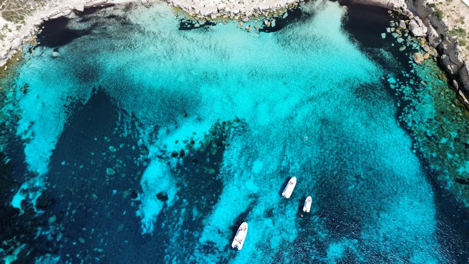 A deep turquoise cove on the Favignana coast with small boats anchored along the rock edge