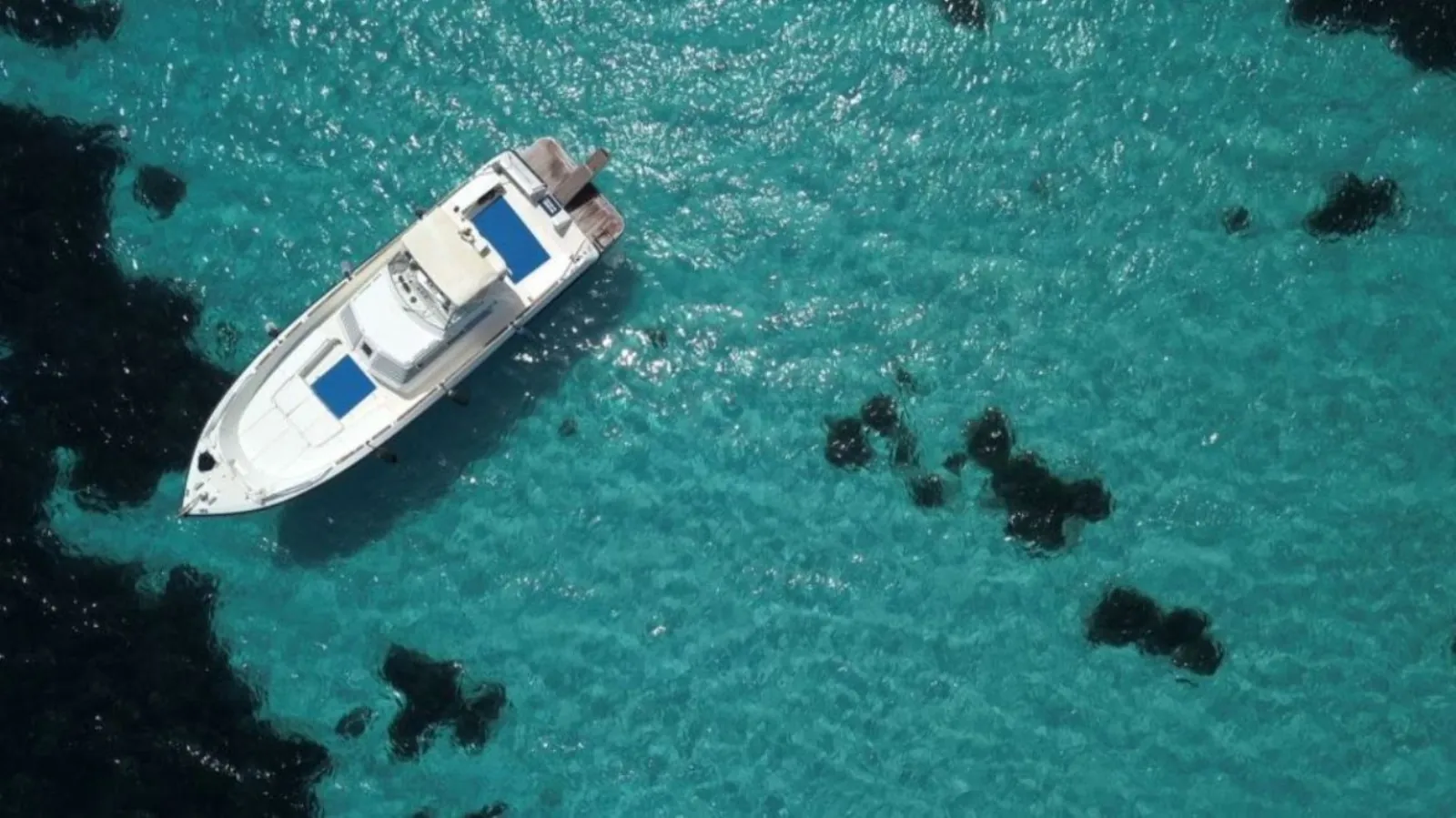 The 14-metre yacht anchored above dark seagrass in shallow turquoise water, seen from the air