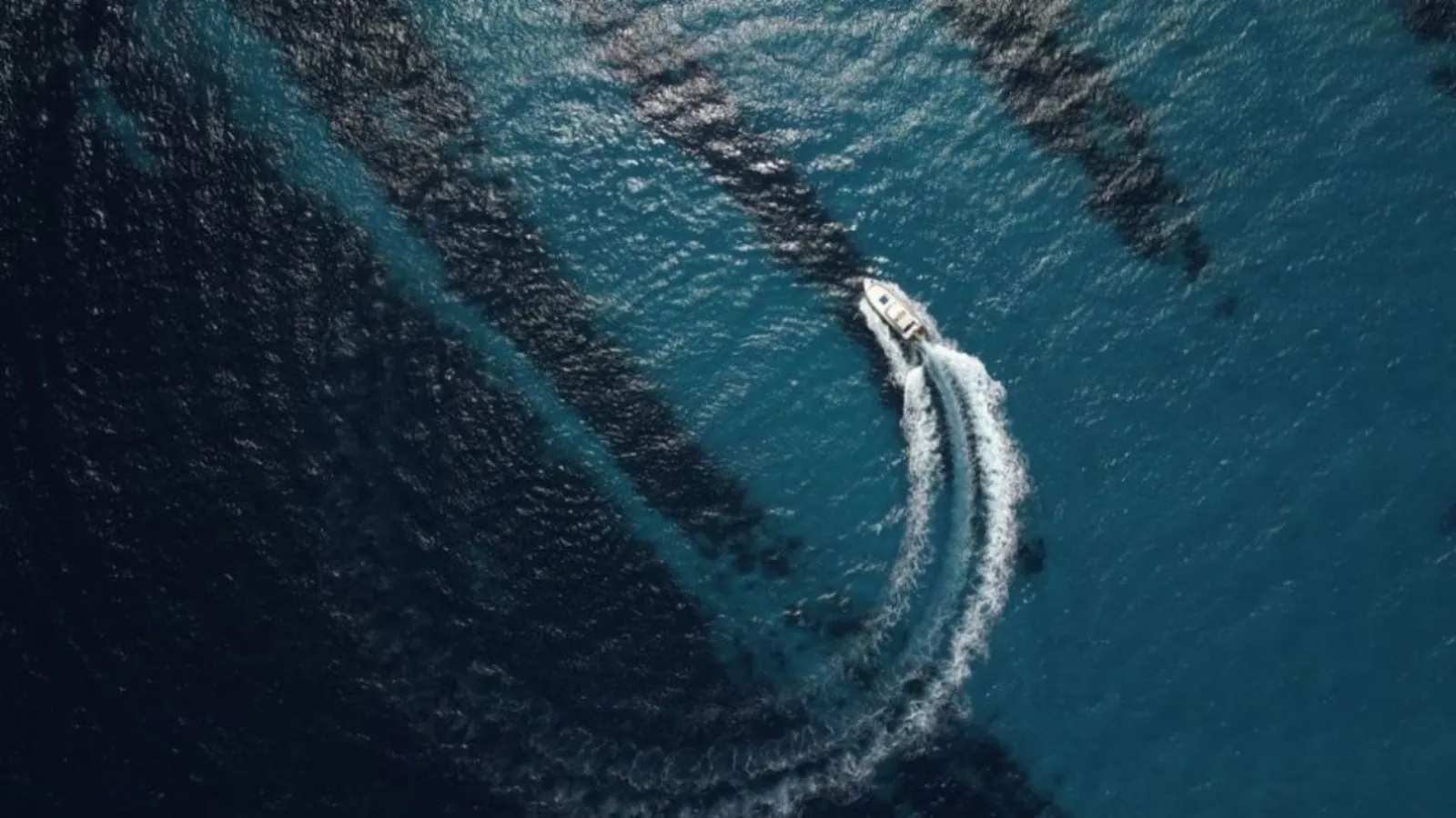 The yacht's wake curving across deep blue water, photographed from above