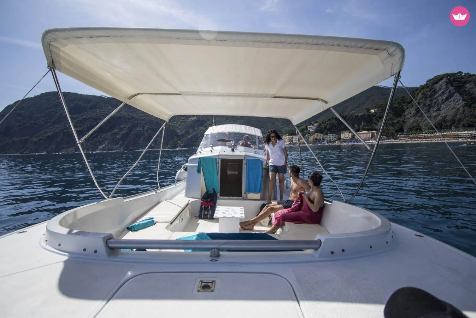 The shaded aft deck under its awning, with guests aboard and the coast behind