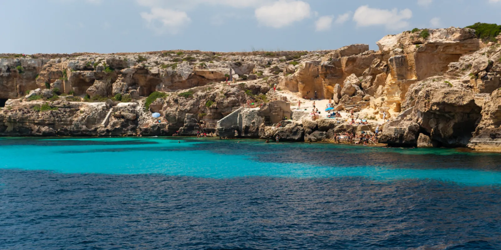 A cliff-backed Favignana cove with sunbathers out on the rocks